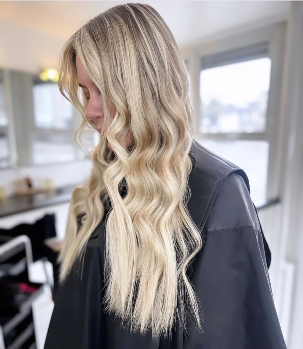 Long honey blonde hair extensions in soft beachy waves, side view in the salon
