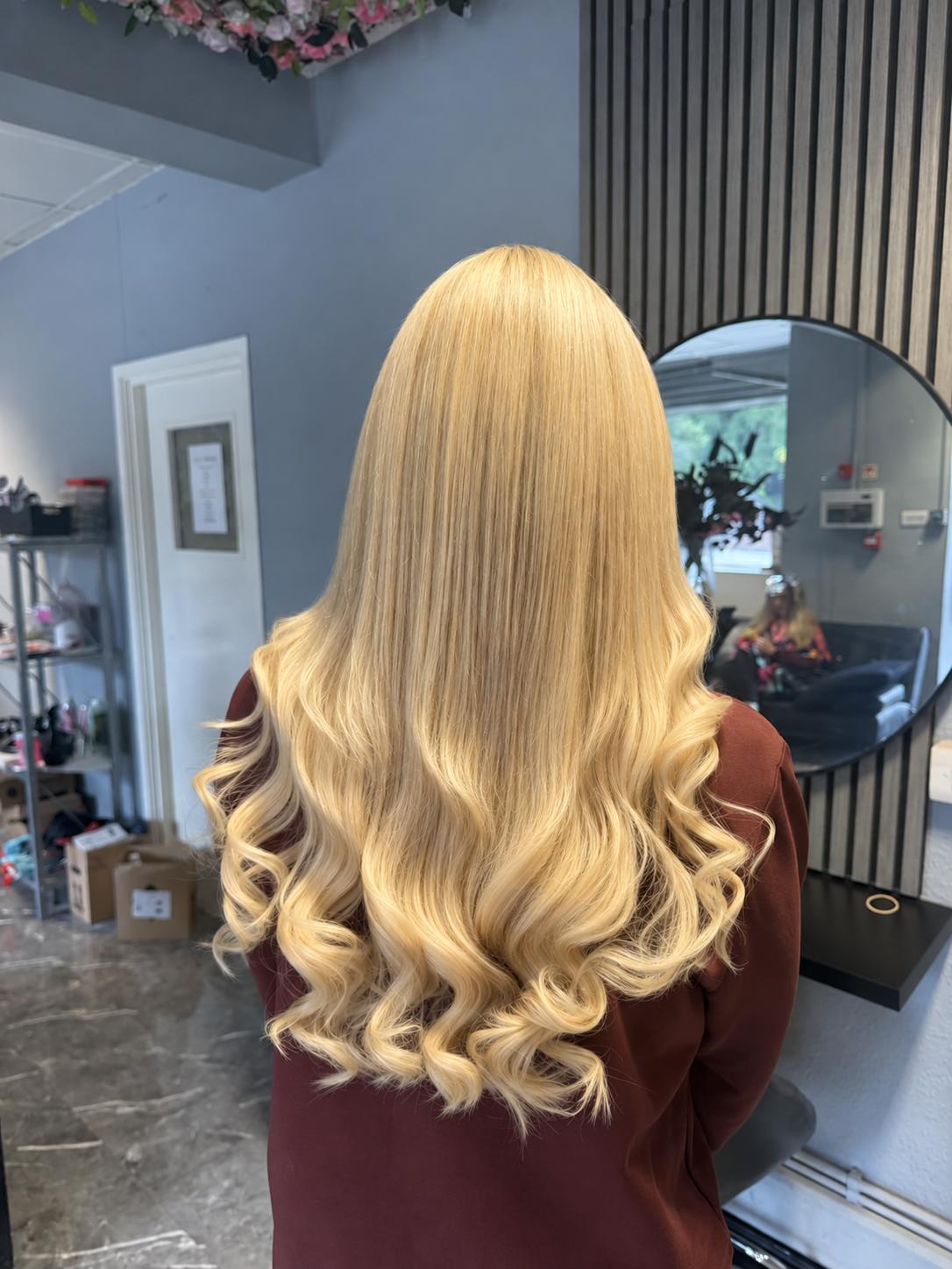 Long, silky blonde hair extensions with soft curled ends, worn in the salon